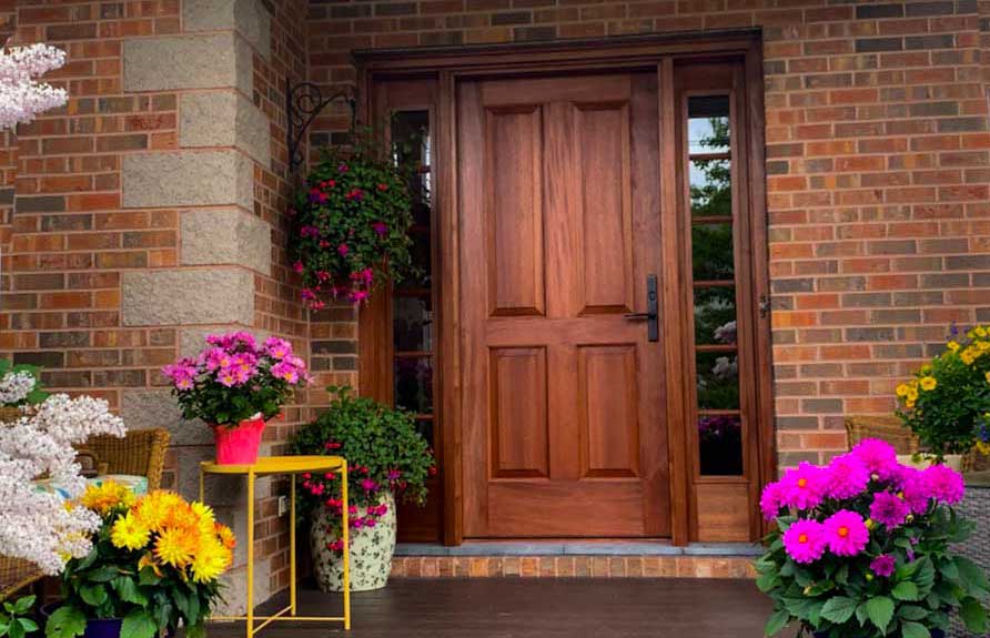Oak front door with black handle. Flowers frame the entrance